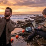 Un uomo cerca visibilità sulla spiaggia mentre uno scienziato finlandese lavora con sensori marini: satira sul contrasto tra rumore, visibilità e competenza.